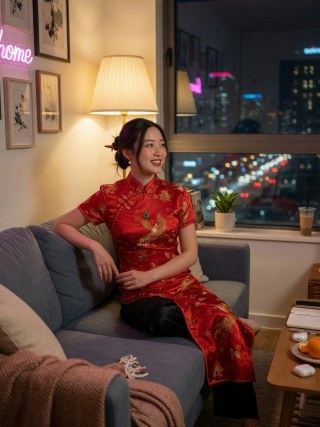 City-night apartment chat in a red qipao with skyline bokeh.